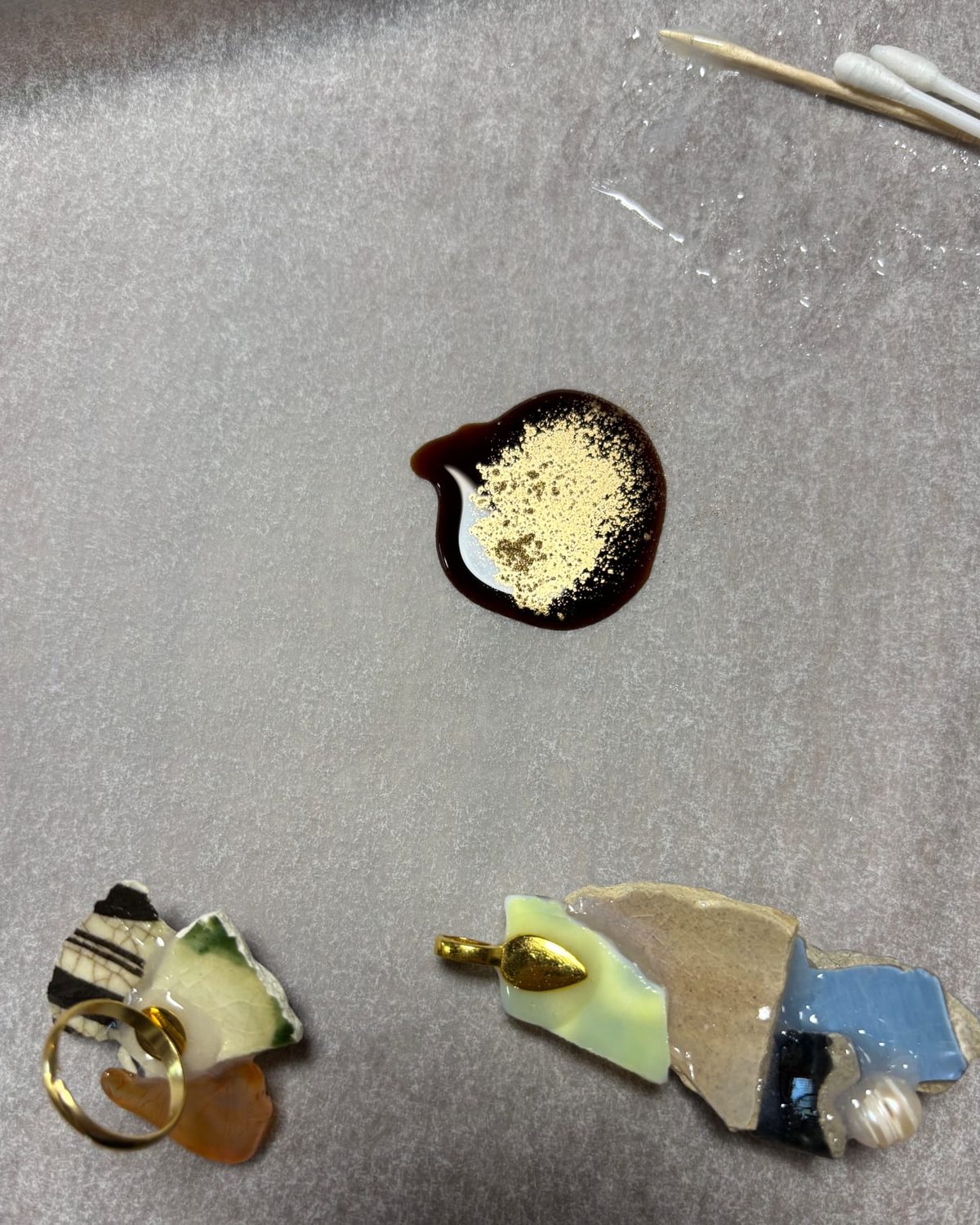 Gold powder mixed into urushi lacquer beside ceramic fragments on Julie's work mat.