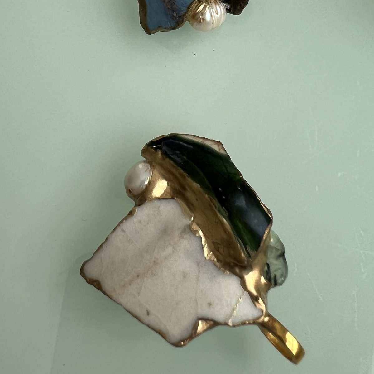 Two kintsugi pendants, one blue and white with a pearl, one dark green and cream.
