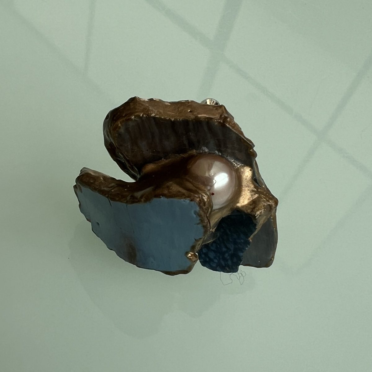 Ring holding a large freshwater pearl between two gold-edged ceramic shards.