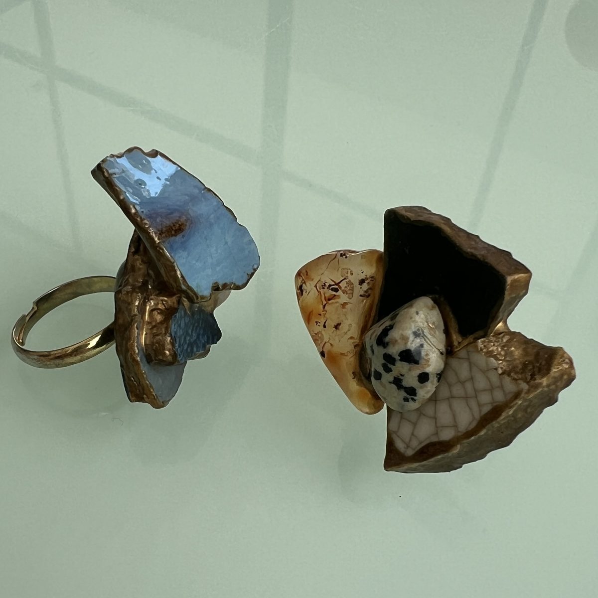 Two finished rings side by side, one blue, one earth-toned, joined with gold.